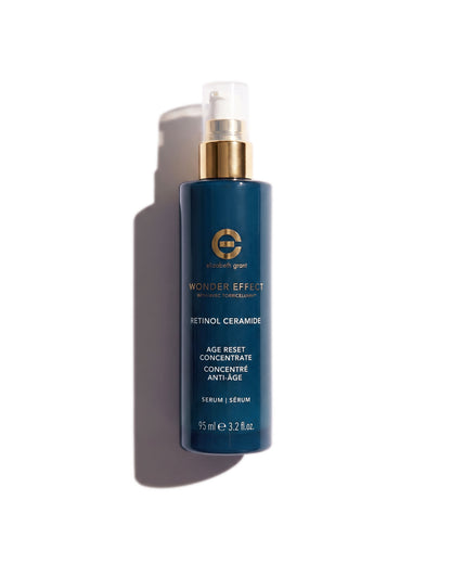 A dark blue cosmetic spray bottle with a gold pump collar and clear cap, labeled &